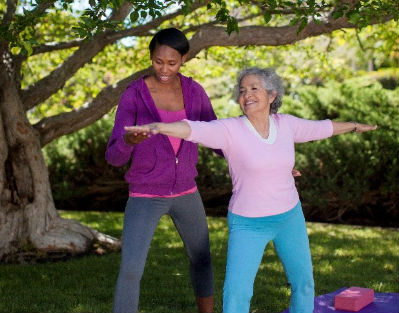 Senior woman wearing pink doing yoga outside with a home care provider in Dallas, TX